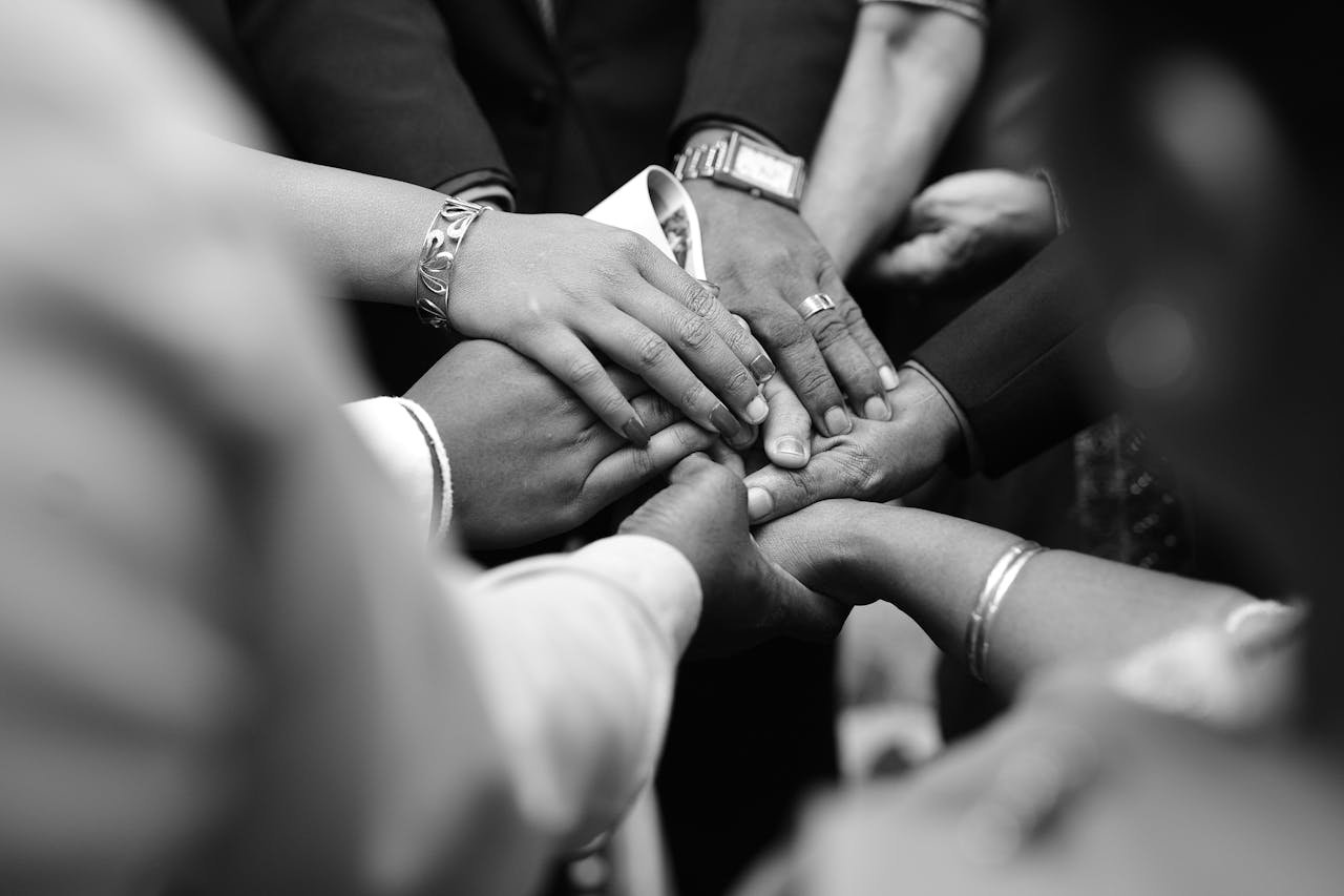 about-us A close-up black and white photo of diverse hands united in prayer, symbolizing spiritual unity.